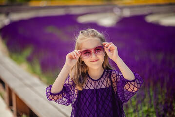 A young girl in a purple dress and sunglasses enjoys the warm sunlight in a field with purple sage