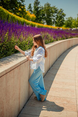 A young girl is basking in the warm rays of the sun, enjoying the beauty of the park, overgrown with bright purple sage. Her white shirt and blue trousers complete the landscape