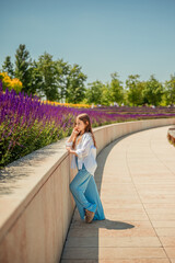 A young girl is basking in the warm rays of the sun, enjoying the beauty of the park, overgrown with bright purple sage. Her white shirt and blue trousers complete the landscape