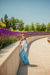 A young girl is basking in the warm rays of the sun, enjoying the beauty of the park, overgrown with bright purple sage. Her white shirt and blue trousers complete the landscape
