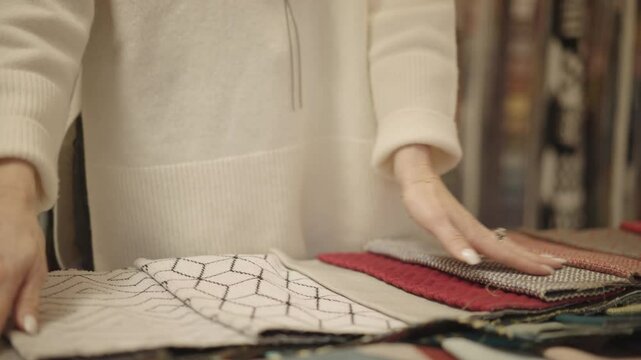 An interior designer's hands delicately explore a variety of fabric samples,  The diverse selection showcases the meticulous process of choosing materials for home decor projects.