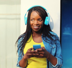 Happy african woman listening to music with smartphone, black girl smiles in headphones holds phone