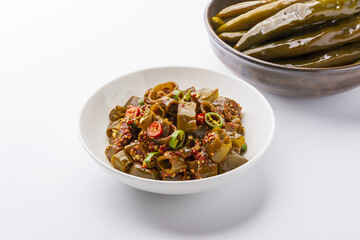 Close-up of seasoned pickled chili peppers with green red pepper pieces and seasonings on pottery bowl and white floor, South Korea
