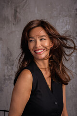 Close-up of an attractive brunette haired woman cheerful smiling against grey wall