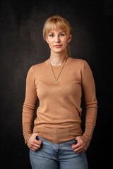 Studio portrait of a blond haired woman standing against isolated dark background