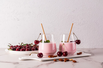 Delicious summer dessert cherry smoothie in a large glass glass with eco straw and a dish with washed ripe cherries by a grey wall.