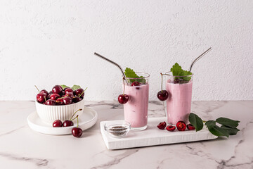 two tall glasses of fresh cherry smoothie or metal straw cocktail on a white wooden plank against a white brick wall. Delicious dessert.