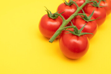 Red cherry tomatoes with green branch on yellow background