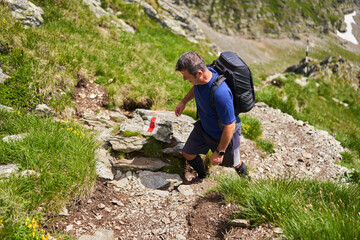 Exhausted hiker with backpack on a trail in the mountains