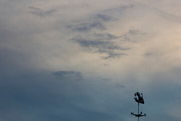 Silhouette of wind vane against the sky with clouds.