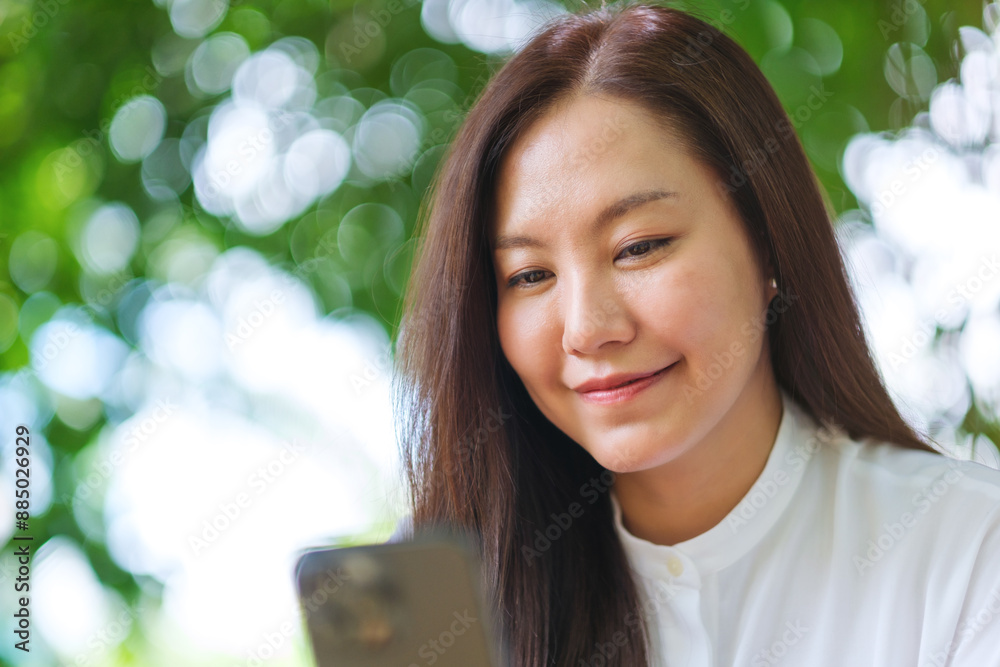 Wall mural portrait image of a young woman holding and using mobile phone in the outdoors