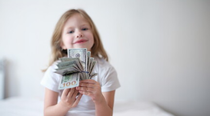 Portrait of little smiling girl counting money, happy childhood. Small cheerful kid holding cash in hands