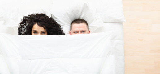 Top view of man and woman covering with white blanket, awake couple in bad. Couple in love hiding...