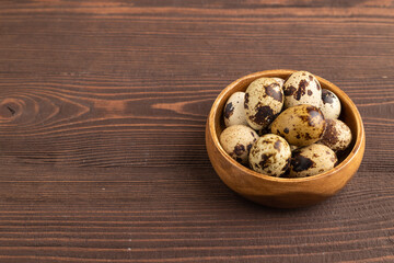 Pile of raw quail eggs in bowl on a brown wooden. side view, copy space.