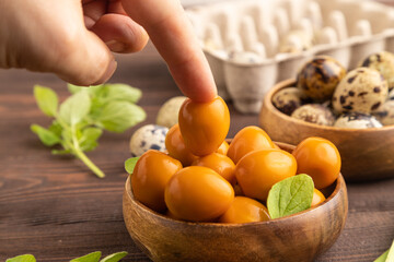 Pile of smoked quail eggs in bowl with hand on a brown wooden. side view, selective focus.