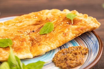 Fried homemade khachapuri cake with cheese and meat, fried in pan on brown wooden. Side view, close up, selective focus