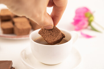 Chocolate marshmallow with cup of coffee with hand on white wooden. side view, selective focus