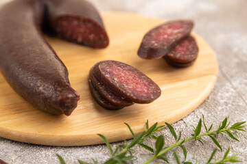 Sujuk sausage on wooden cutting board with pepper and herbs on brown concrete. Side view, selective focus.
