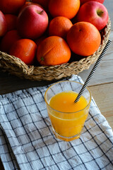 One glass of orange juice is standing on the wooden table with a basket of oranges in the background. Eating healthy every day. Orange juice and oranges