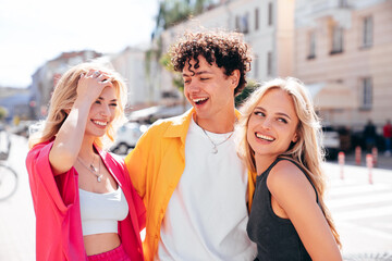 Obraz premium Group of young three stylish friends posing in the street. Fashion man and two cute female dressed in casual summer clothes. Smiling models having fun. Cheerful women and guy outdoors