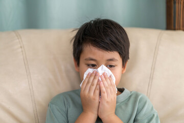 Young asian boy sneezing or blowing his nose and mouth with tissue, cold allergies or illness, health, virus and flu season, RSV, Influenza, childcare and hygiene practices, especially for children