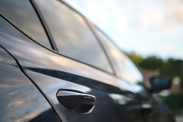 Fototapeta premium Blurred side view of a car parked in a driveway, focusing on the rear door handle, with perspective effect.