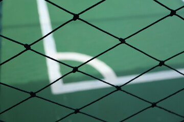 Fototapeta premium a close-up of a black chain-link fence with a blurred background featuring a green sports court with white boundary lines.