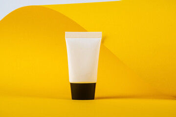 Plastic white tube for cream or lotion. Skin care or sunscreen cosmetic with stylish props on yellow background.