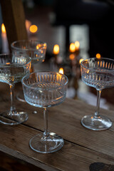 Shiny glass transparent glasses on a tall stem with a transparent drink, in the dark against the background of candle lights