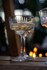 Shiny glass transparent glasses on a tall stem with a transparent drink, in the dark against the background of candle lights