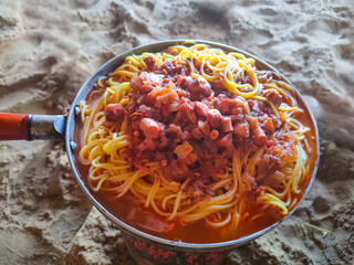 Close up of a pan in which seafood spaghetti is prepared during summer camping at the beach. El Tarf