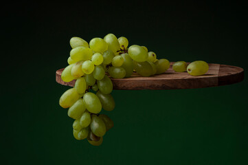 bunch of grapes, yellow-green fruits on a wooden tray, floating effect on a gradient dark green background