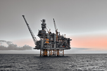 Offshore oil and gas jackup platform in the ocean during sunset in grey colours. 