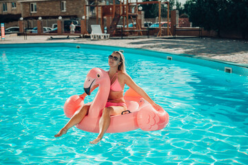 Naklejka premium A woman is sitting on a pink inflatable flamingo in a pool. Concept of fun and relaxation, as the woman is enjoying her time in the water