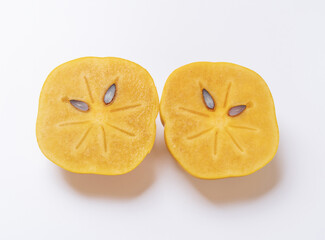 Close-up and top angle view of two sweet persimmon fruits with half cut on white floor, South Korea
