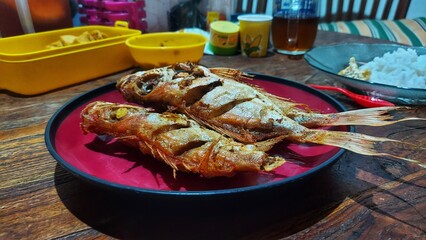 Fried fish placed on a plate isolated on a wooden background.