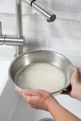 Woman holding bowl with rice and water above sink, closeup