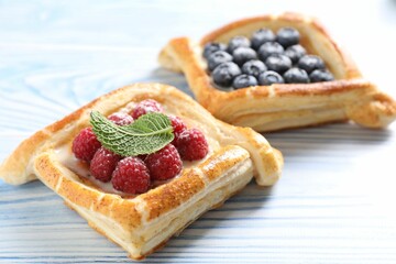 Tasty puff pastries with berries on light blue wooden table, closeup
