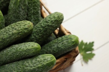 Fresh green cucumbers in wicker box on white table, closeup