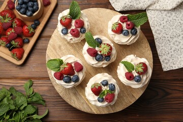 Tasty cupcakes with different berries and mint on wooden table, flat lay