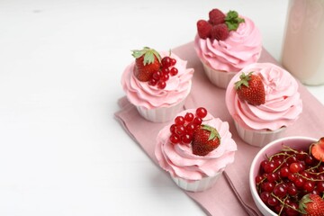 Tasty cupcakes with strawberries and red currants on white table, space for text