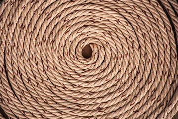 Fototapeta premium Brown rope with red lines and coiled roll from top view on wooden table background in warm tone. Braided rope on a roll background texture 2025. Photo of an old vintage rope.