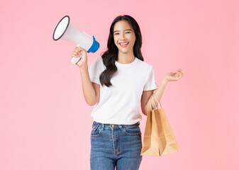Beautiful Asian woman holding megaphone and brown blank craft paper bag on pink background.