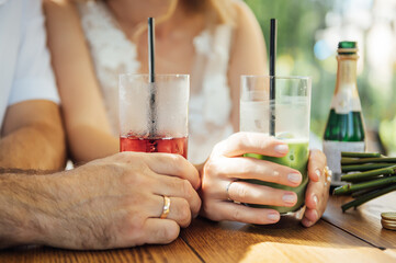 Couple drinking cocktail with slice of orange. Bride and groom holding cocktails. Honeymoon concept after wedding.