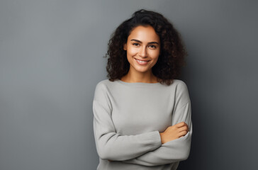 Obraz premium Confident Young Woman with Curly Hair Smiling and Standing Against a Neutral Gray Background