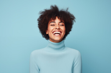 Obraz premium Happy woman in a light blue turtleneck sweater, laughing joyfully against a matching blue background, capturing a moment of pure happiness