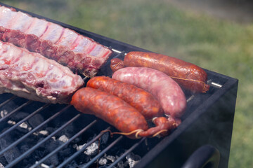 Image of raw pork ribs spread out on a grill, above glowing charcoal, set against an outdoor backdrop illustrating preparation of a traditional barbecue meal.