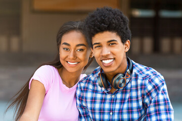 This image shows a teen black couple smiling and looking at the camera. They are both dressed casually and appear to be happy. The image is likely taken outdoors in the daytime