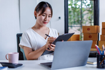 Portrait business woman smile and use tablet checking information on parcel shipping box before send to customer. Entrepreneur small business working at home. SME business online marketing.
