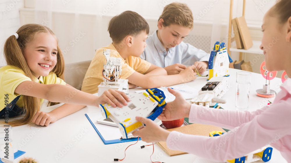 Poster Four students, three girls and one boy, work together to build a robot during a STEM class. The students are all smiling and engaged in the activity, demonstrating their interest in science